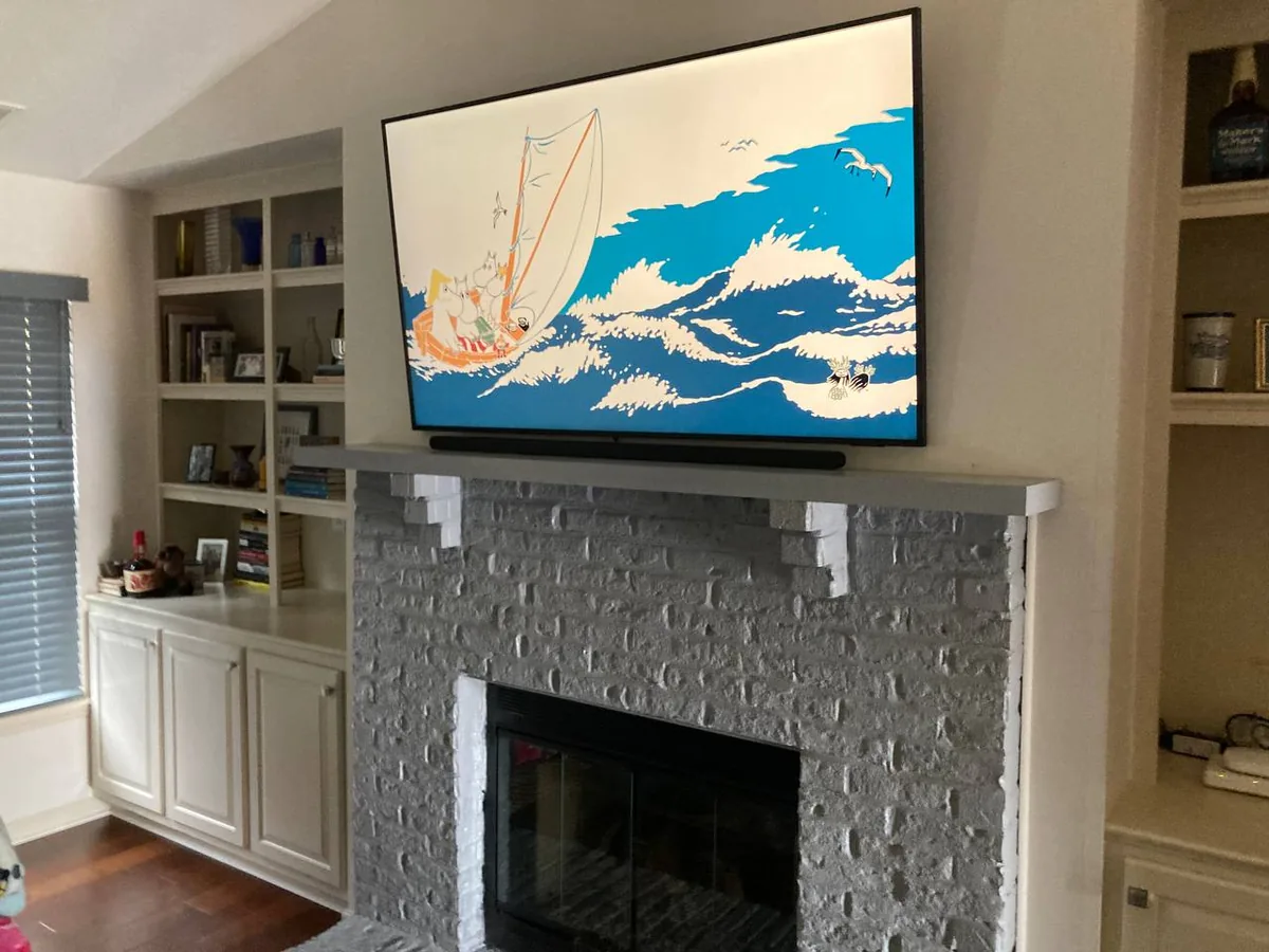 65-inch Samsung TV mounted over brick fireplace with hidden wiring and built-in shelving
